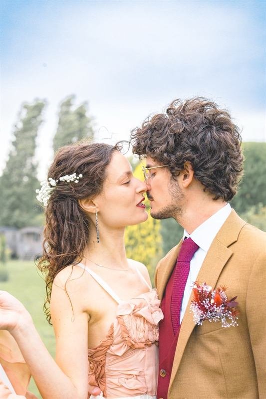 Mariés s'embrassant en extérieur, la mariée en robe rose poudré, le marié en costume camel