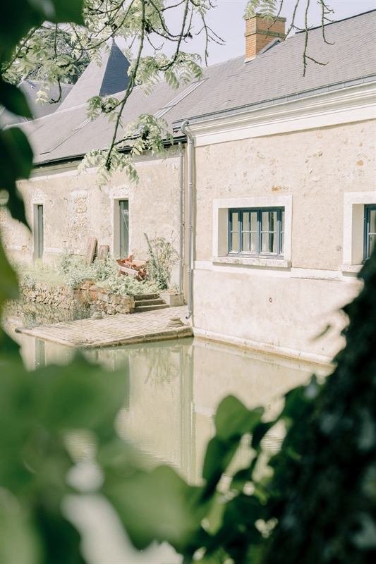 Façade en pierre d'une demeure ancienne se reflétant dans l'eau, à travers le feuillage