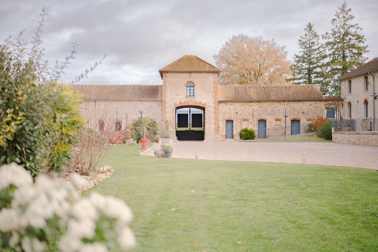 Cour d'un domaine de réception en pierre, pelouse et fleurs blanches au premier plan