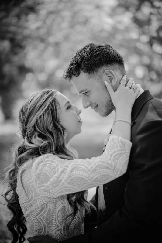 En noir et blanc, la mariée caresse le visage du marié