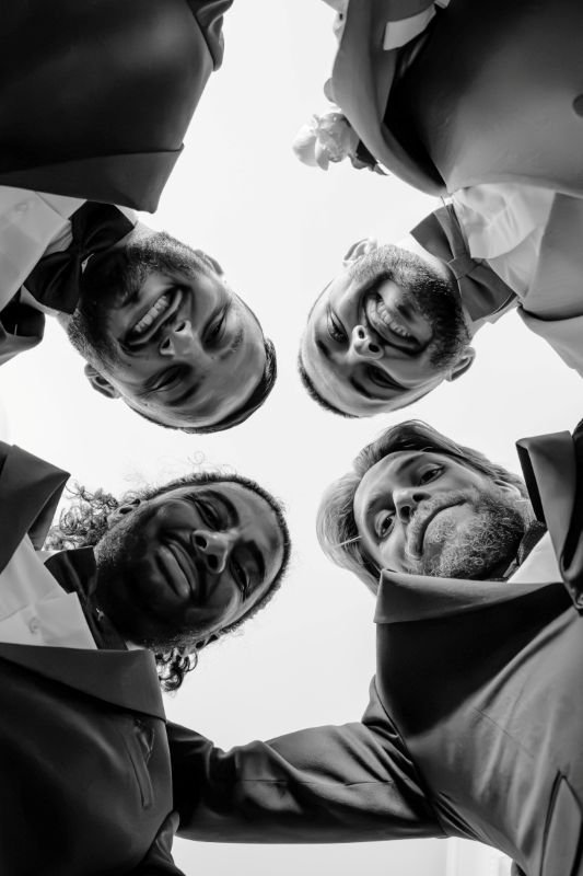 En noir et blanc, quatre hommes penchés vers l'objectif, photographiés d'en dessous