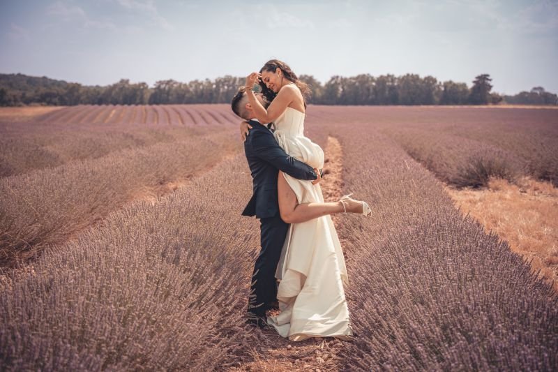 Dans un champ de lavande, le marié soulève la mariée pour l'embrasser