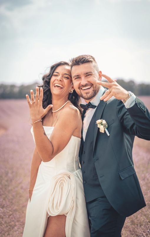 Les mariés éclatent de rire en montrant leurs alliances au milieu d'un champ de lavande