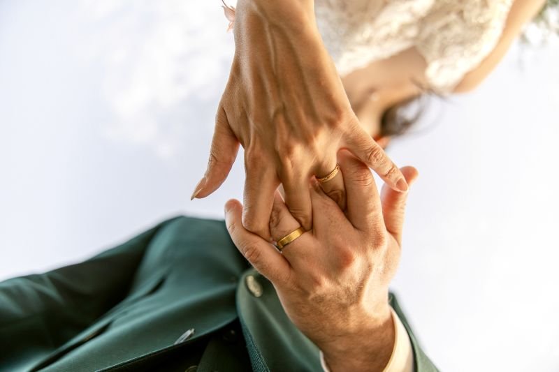 Les mains des mariés et leurs alliances, sur fond de ciel clair