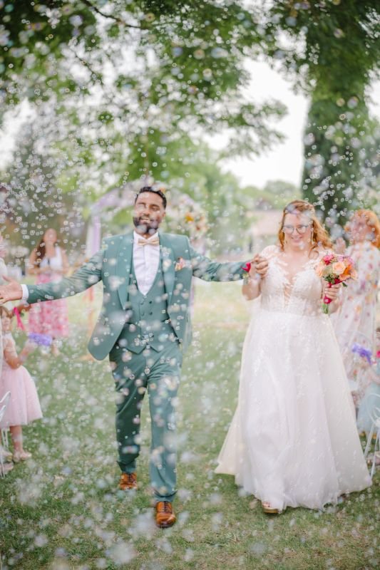 Sortie de cérémonie sous une pluie de confettis, les mariés rayonnants au milieu des invités